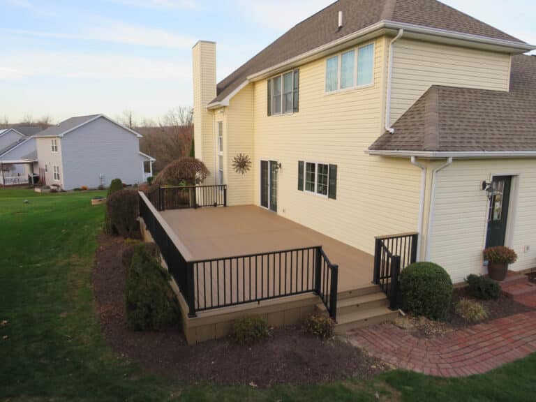 A 12x20 deck with black railings and stairs leading down in the back of a white house in the morning