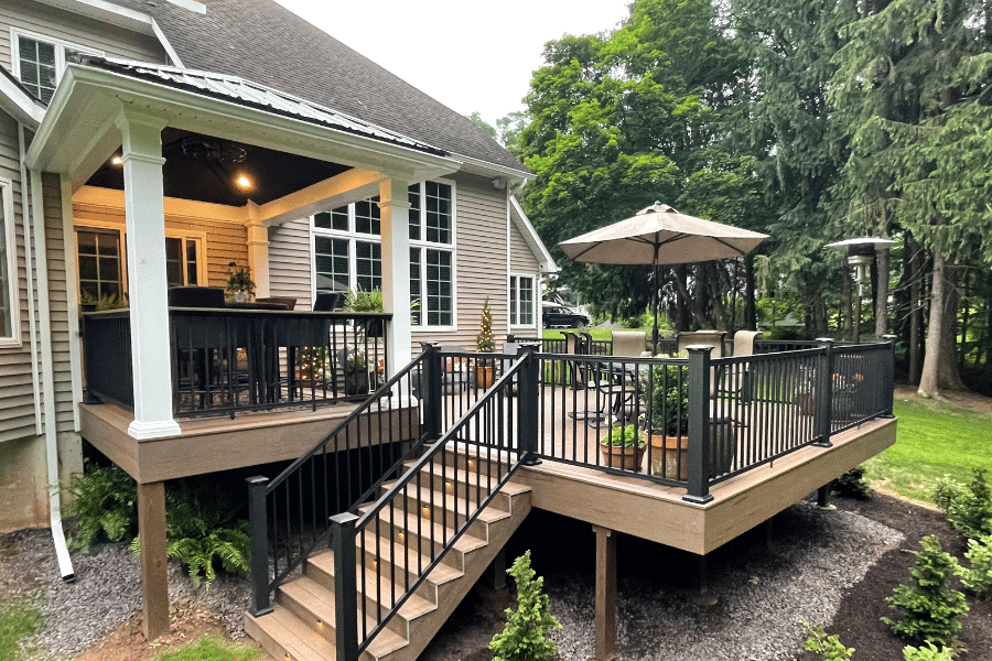 light brown wood composite decking with overhang ocer part of it and chairs with umbrella on lower level featuring lights in stairs leading up to it